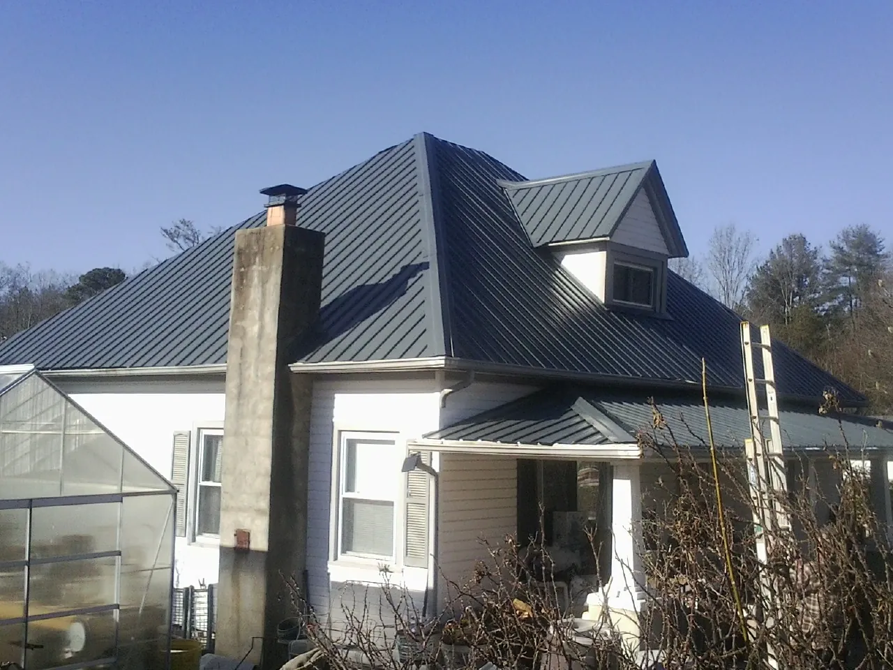 Dark blue standing seam metal roof on a white farmhouse with dormer — Slate & Tile Roof Repair by Roofing Brothers in Allgood