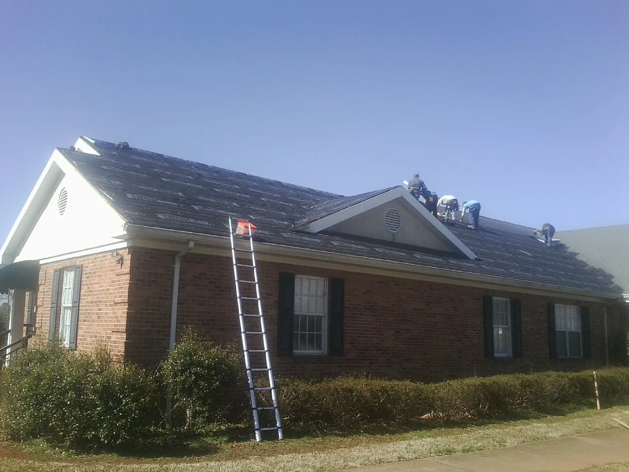 Crew tearing shingles off a brick ranch roof with a ladder set — Metal Roof Repair work by our crew in Allgood