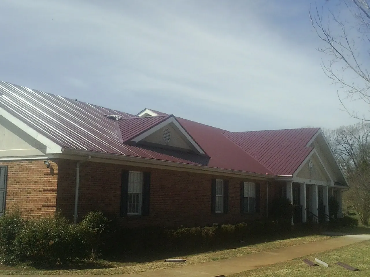 Red metal roof with gabled entries on a long brick building, from a Hail Damage Roof Repair job in Allgood