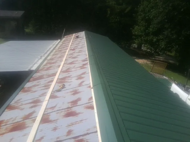 Old rusted panels beside newly installed green metal roofing — Wind Damage Roof Repair by Roofing Brothers in Allgood