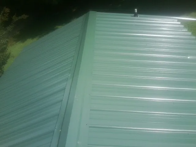 New green metal panels meeting at the ridge of a roof — Flat Roof Repair work by our crew in Allgood