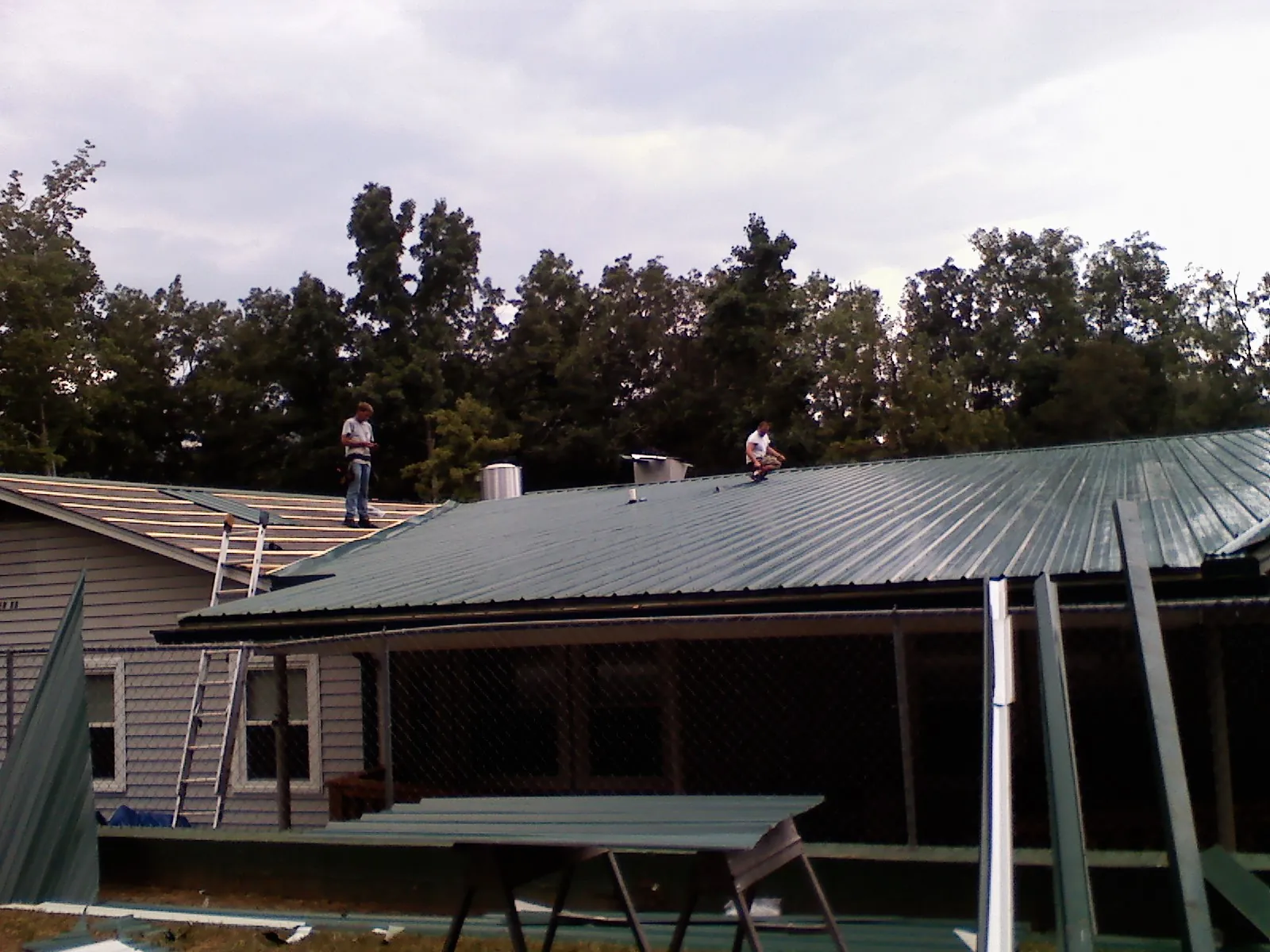 Two roofers installing green metal panels above a covered porch in Allgood