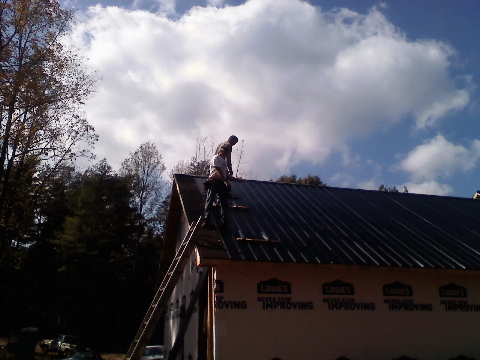 Roofer fastening dark metal panels high against a cloudy sky, from a Roof Inspection job in Allgood