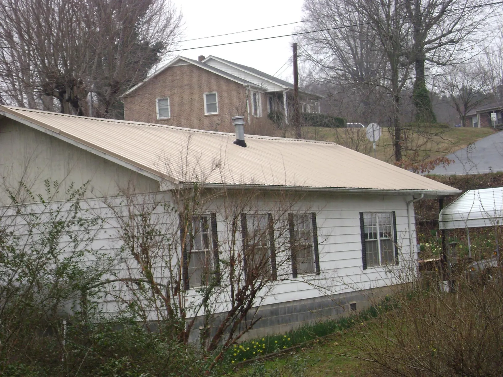 Tan metal roof on a white sided house set into a hillside — Commercial Roofing by Roofing Brothers in Allgood